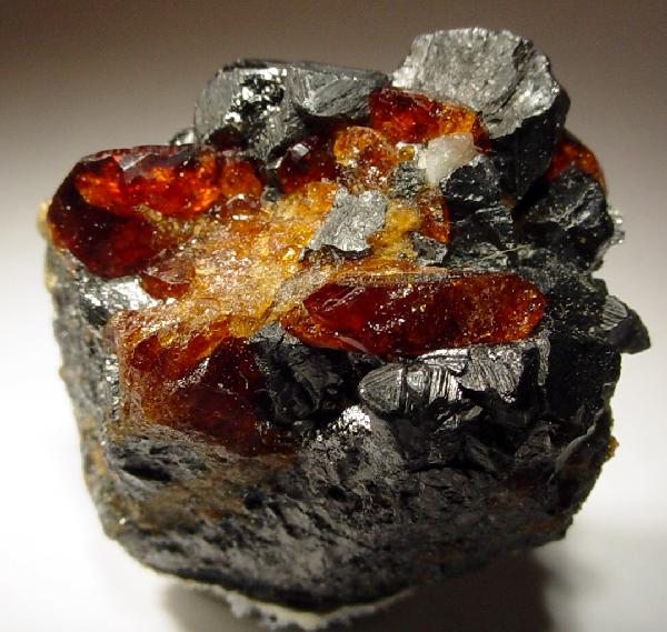 A shiny black chunk of pyramidal magnetite with glittering red crystals of chondrodite on top