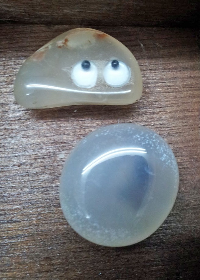 A round, translucent light blue stone with a dark blue wisp within. Next to it is an oblong off-white stone with two googly eyes glued on.