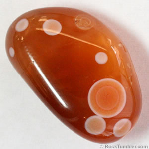 A shiny, smooth orange stone with white concentric circles, some overlapping one another.