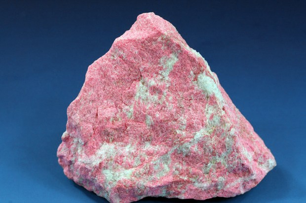 A roughly triangular chunk of rock covered with bubblegum-pink splotches.  They sparkle slightly against the contrasting blue background.