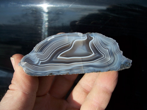 A person holding a trapezoid-shaped agate with dark blue, black, and white bands that appear to have depth.  