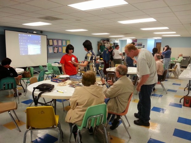 About 15 people sitting or standing, looking at rocks and talking to one another.