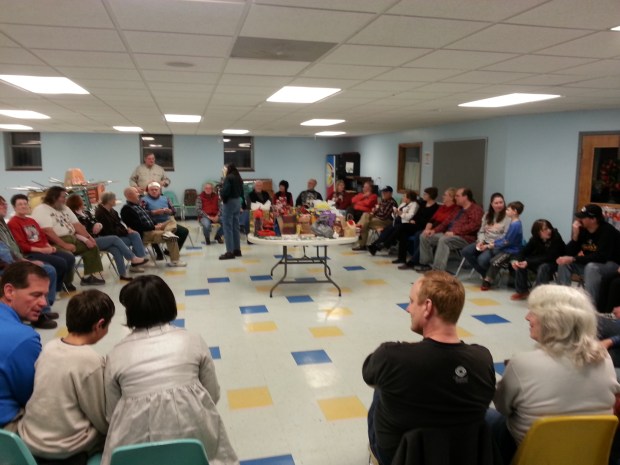 Lots of people sitting in a circle around a table full of wrapped gifts.
