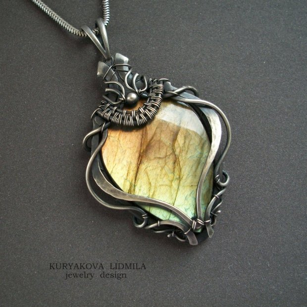 A shimmery orange, yellow, and green laboradite cabochon in a burnished gray metal wire wrapped setting and necklace chain.