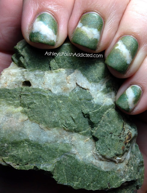 A hand with green and white banded fingernails that perfectly match the green and white banded rock it is holding.