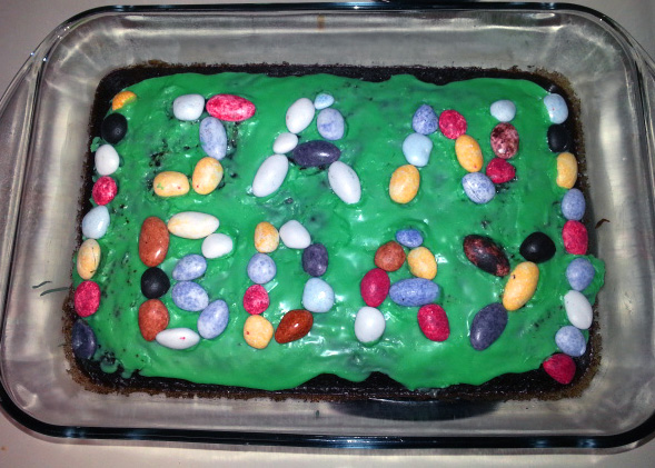 A chocolate cake with green icing and multicolored rocks spelling 