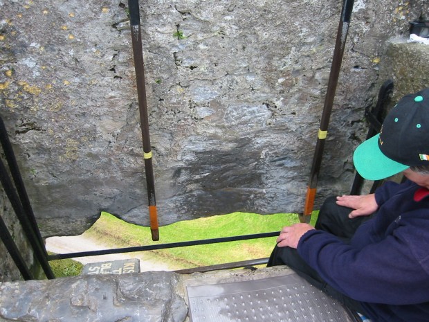 The Blarney Stone looks like a big gray stone with a metal railing attached. You can see the ground far below. 