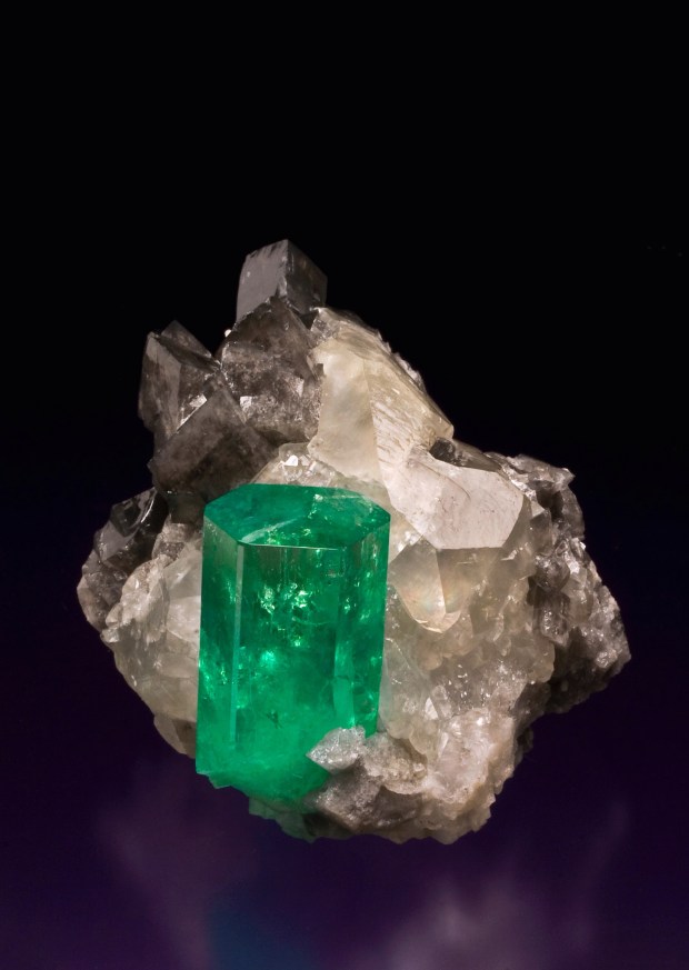 A rectangular green emerald crystal sticking out of a white and gray calcite crystal matrix.