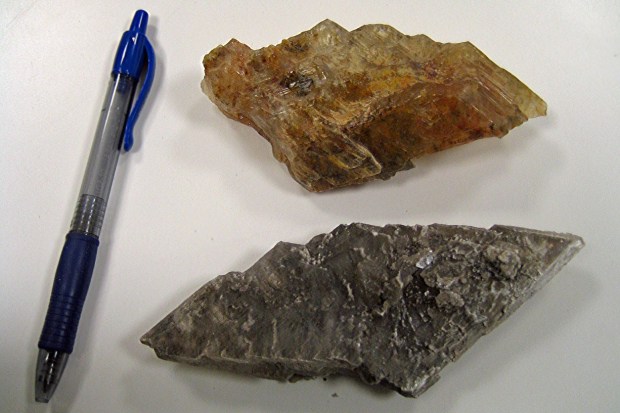 Gray selenite crystal and orange selenite crystal, both about the size of a ballpoint pen.
